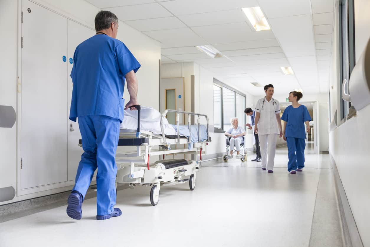 Male nurse pushing a stretcher bed in a hospital corridor with fellow doctors